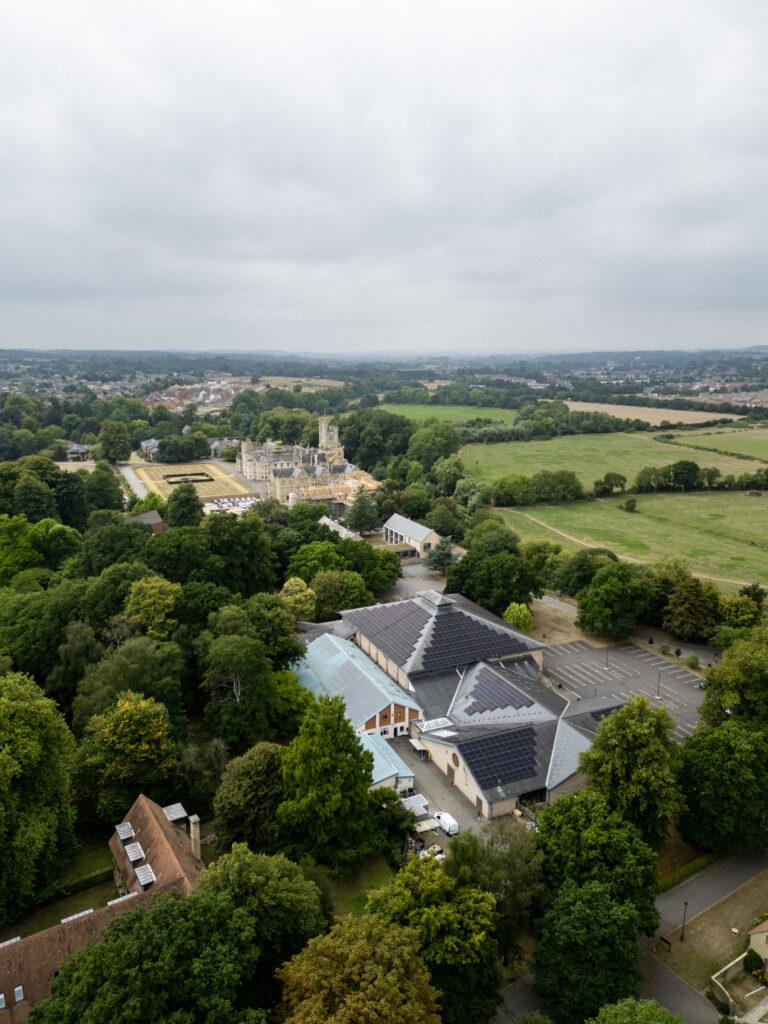 Aerial view of a property with several buildings surrounded by dense trees and open fields under a cloudy sky.