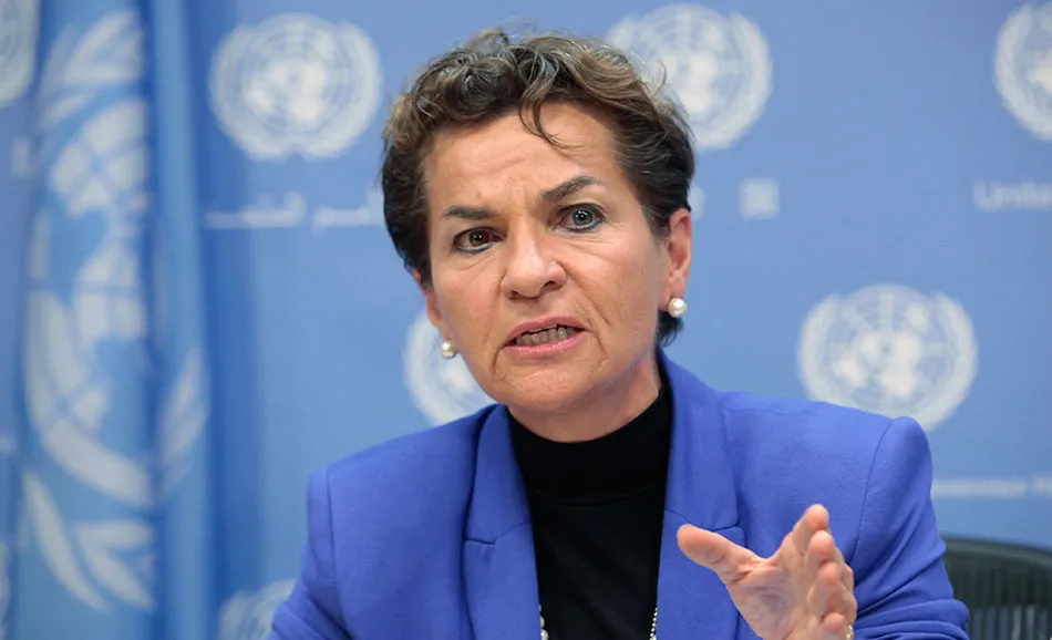 Christiana Figueres speaks at a press conference, gesturing with her hand, with a United Nations backdrop behind her.