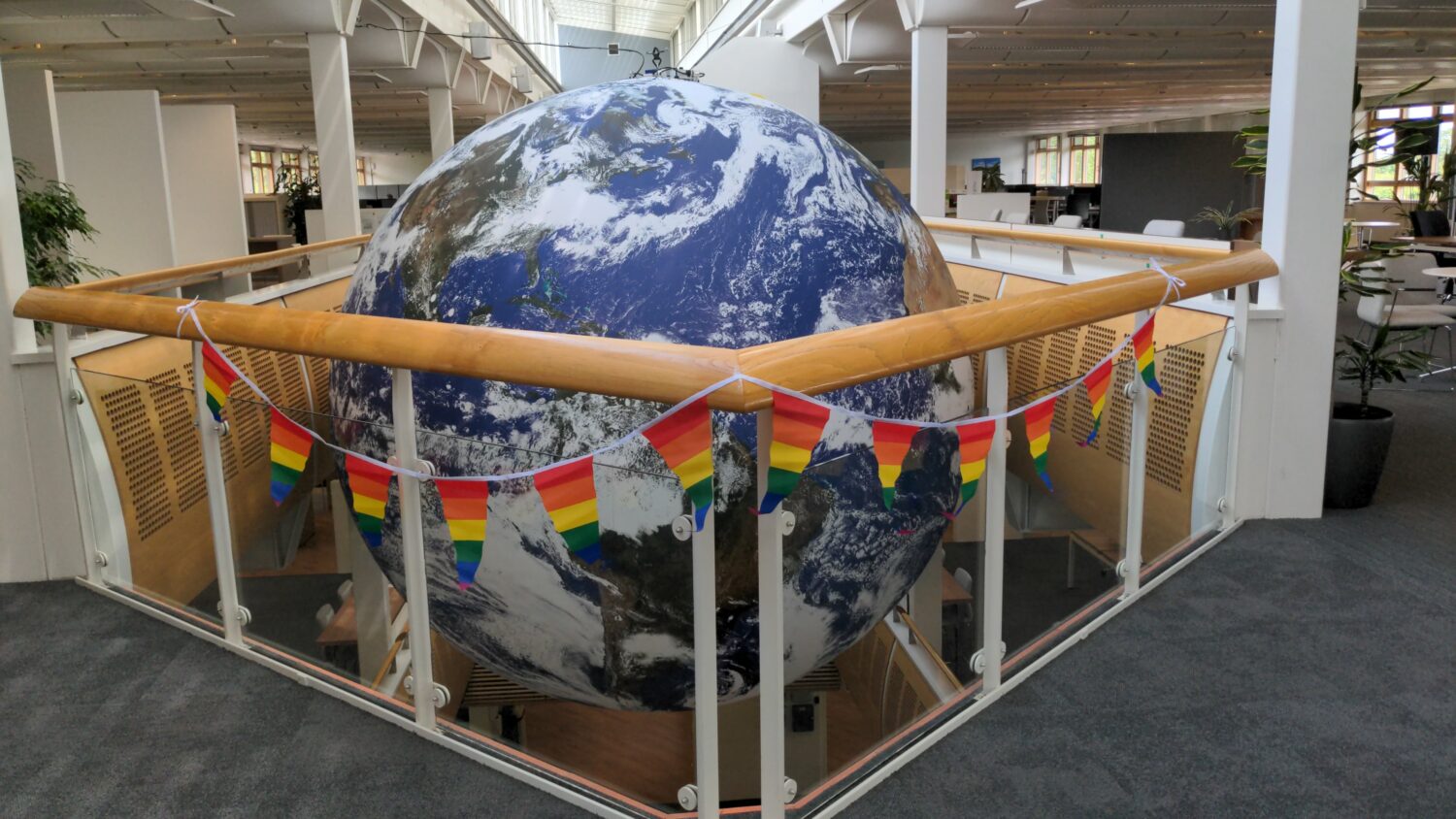 Rainbow LGBTQ+ pride flags in front of a sculpture of the earth.