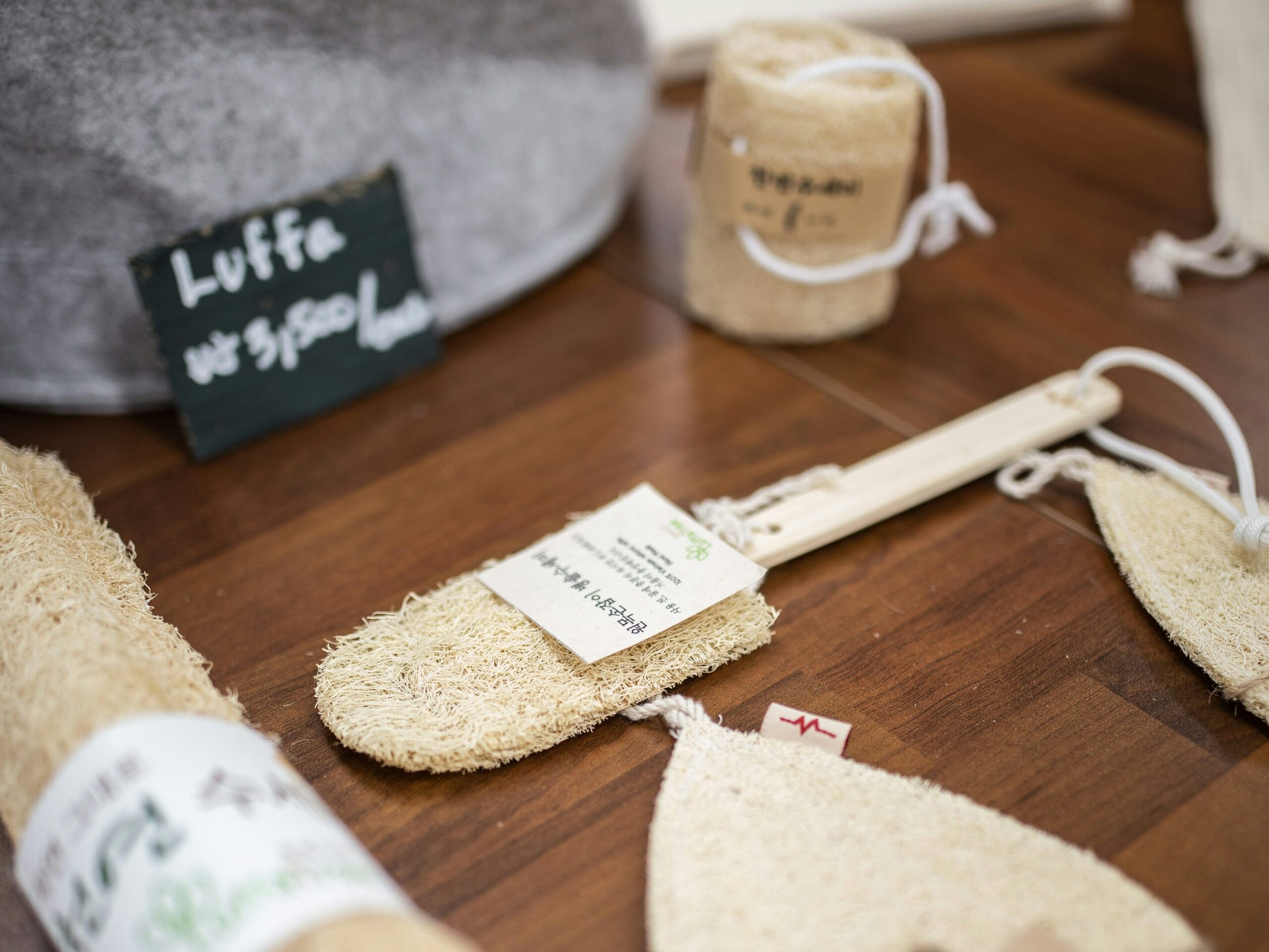Various natural loofah sponges and brushes are displayed on a wooden table next to a handwritten label reading Luffa, perfect for those embracing eco-friendly living.